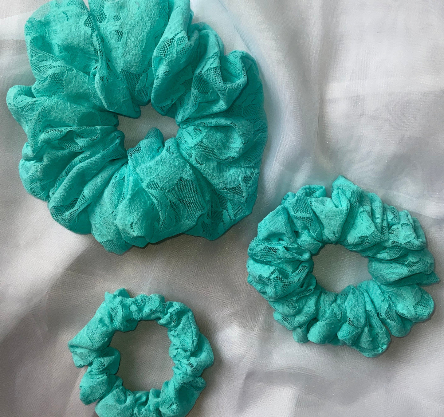 Three turquoise lace hair scrunchies of different sizes placed on a white surface.